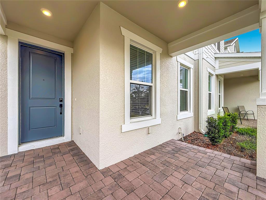 A covered entryway features a blue front door, a window, and brick paver flooring — 13568 AUTUMN HARVEST AVENUE, WINTER GARDEN, FL