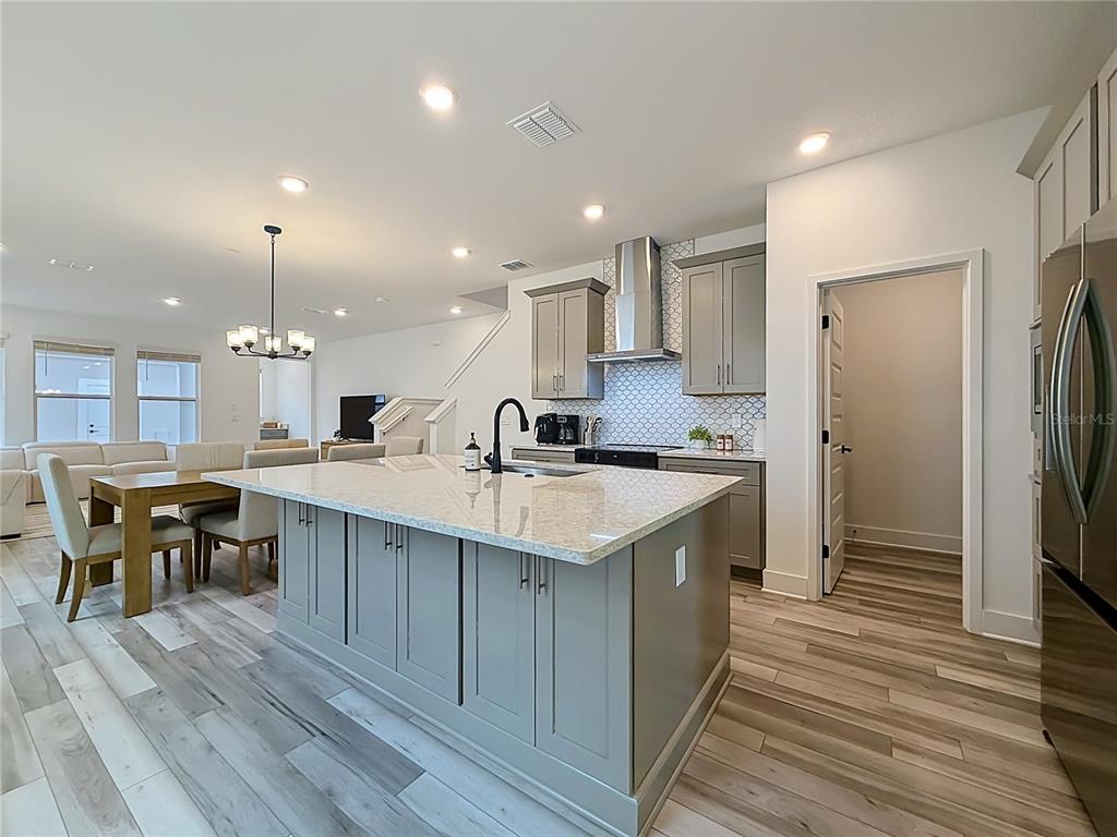 A modern kitchen features a large gray island, granite countertops, and light wood-look flooring — 13568 AUTUMN HARVEST AVENUE, WINTER GARDEN, FL