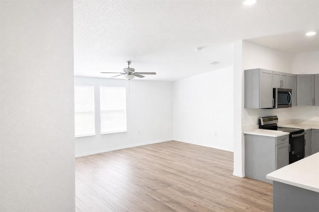 An open-concept living area with light wood-look flooring and a kitchen with gray cabinets — 10121 EVANSTON LANE, WESLEY CHAPEL, FL