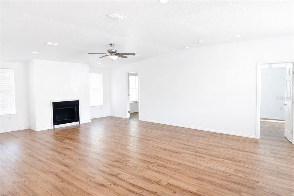 A bright living room features light wood-look flooring, a fireplace, and a ceiling fan — 10121 EVANSTON LANE, WESLEY CHAPEL, FL