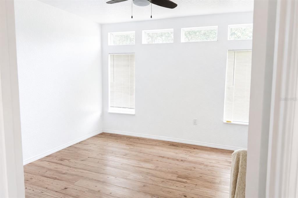 An empty room with light wood-look flooring, white walls, and four windows with blinds — 10121 EVANSTON LANE, WESLEY CHAPEL, FL