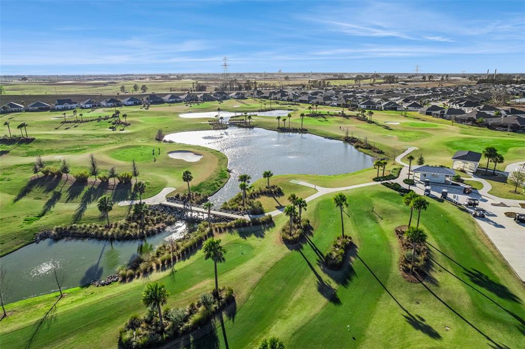 An aerial view of a golf course featuring a large pond, palm trees, and houses — 7492 FAR HILLS LOOP, THE VILLAGES, FL