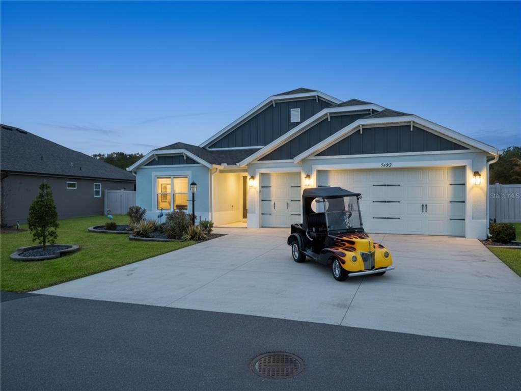 A single-story house with a blue exterior, a three-car garage, and a flame-painted golf cart — 7492 FAR HILLS LOOP, THE VILLAGES, FL