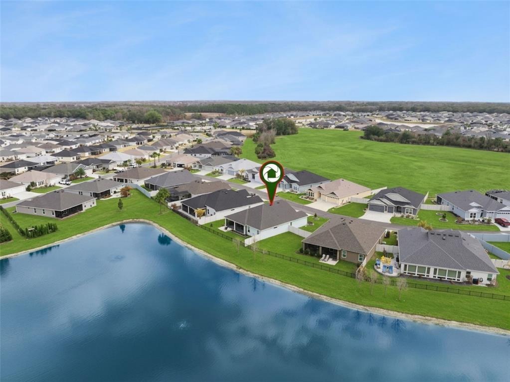 An aerial view shows a suburban house with a backyard pool cage facing a lake — 7492 FAR HILLS LOOP, THE VILLAGES, FL