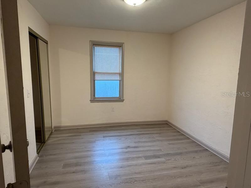 An empty bedroom features light-colored wood-look flooring, off-white walls, a window, and a mirrored closet — 4255 43RD AVENUE N, ST PETERSBURG, FL