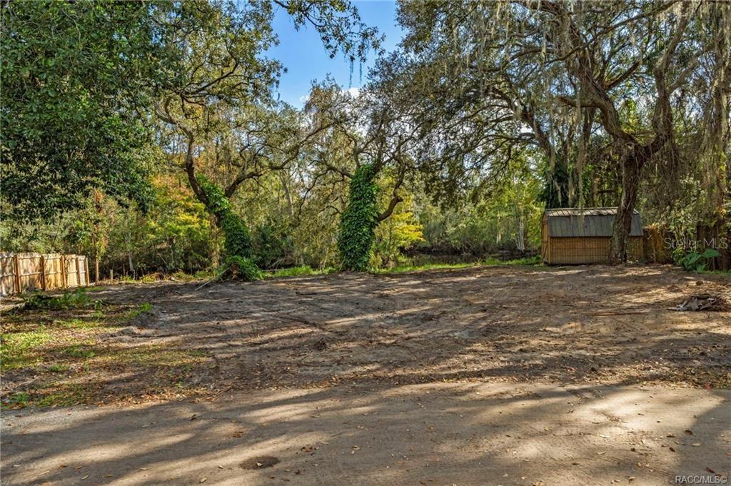 A cleared, vacant lot features mature trees, a small shed, and a wooden fence — 11860 E CARDINAL PLACE, FLORAL CITY, FL
