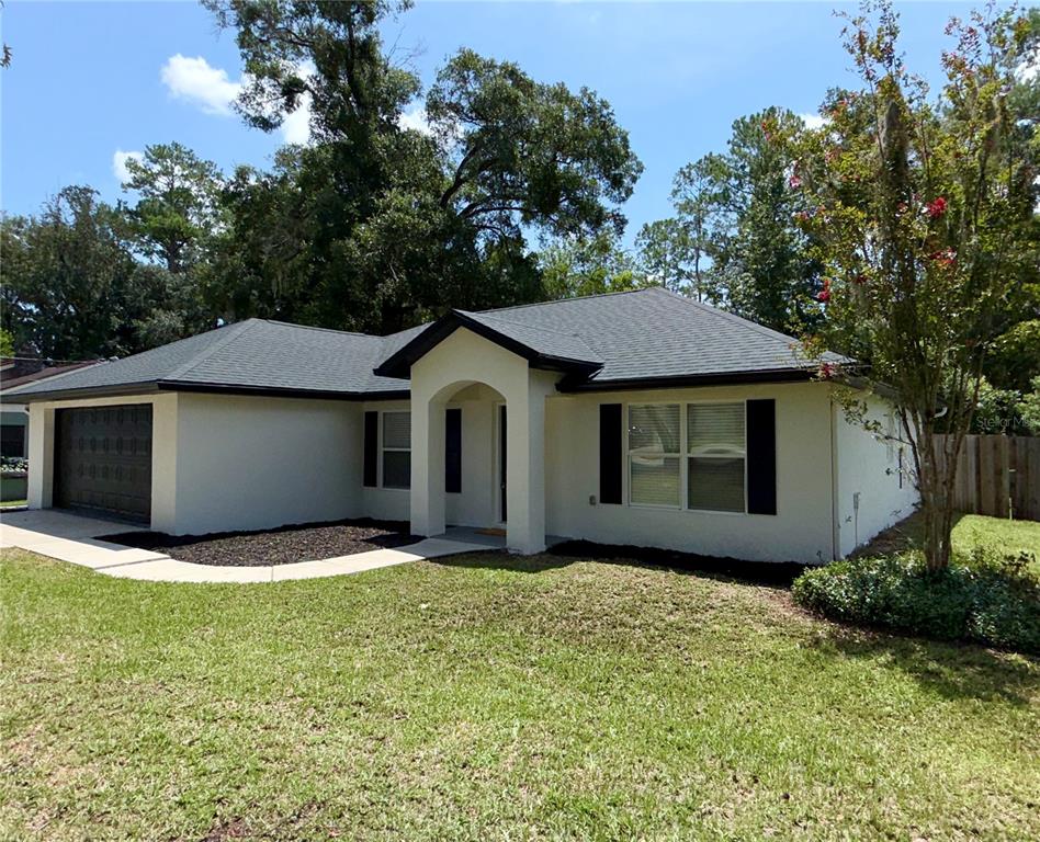 A single-story house with a light-colored stucco exterior, dark roof, and an attached garage — 6150 SE 122ND LANE, BELLEVIEW, FL