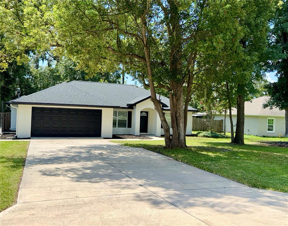 A single-story house with a black garage door and a concrete driveway under large trees — 6150 SE 122ND LANE, BELLEVIEW, FL