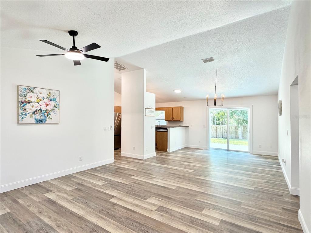 An open-concept living and dining area features wood-look flooring, a ceiling fan, and sliding doors — 6150 SE 122ND LANE, BELLEVIEW, FL