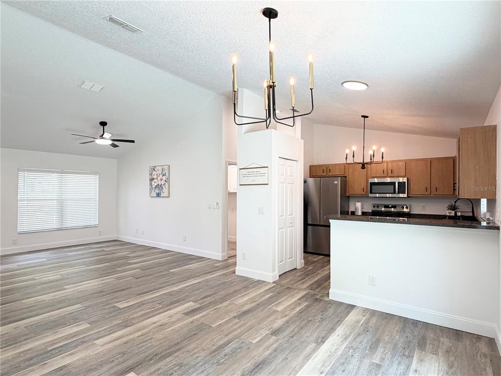 An open-concept kitchen and living area feature wood-look flooring, white walls, and two chandeliers — 6150 SE 122ND LANE, BELLEVIEW, FL