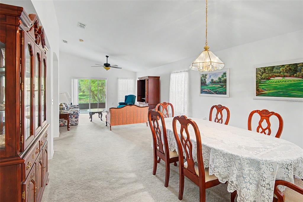 A dining area with a lace-covered table leads into a living room with carpeted floors — 364 ACADIA DR, POINCIANA, FL