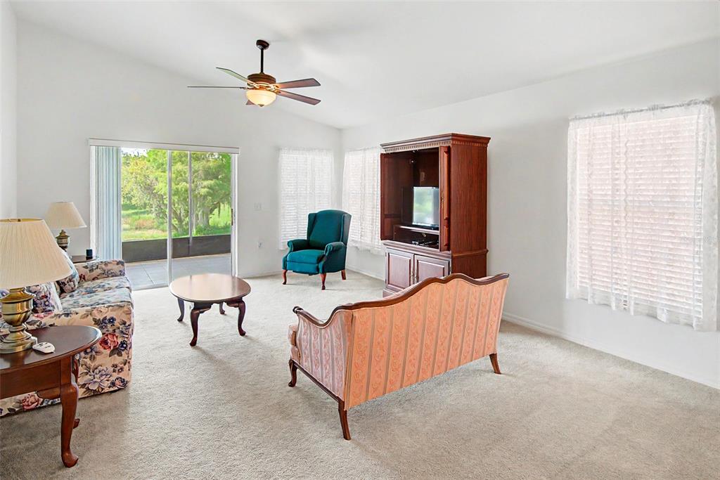 A living room features a floral sofa, a striped settee, a teal armchair, and carpeted floors — 364 ACADIA DR, POINCIANA, FL