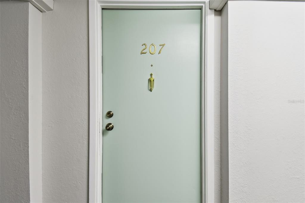 A light green apartment door with the number 207 and a gold-colored door knocker — 255 DOLPHIN POINT UNIT 207, CLEARWATER BEACH, FL