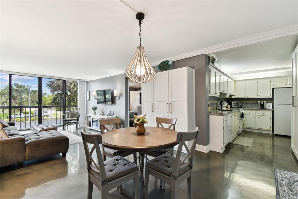 An open-concept living and dining area features polished concrete floors, a beaded chandelier, and kitchen — 255 DOLPHIN POINT UNIT 207, CLEARWATER BEACH, FL