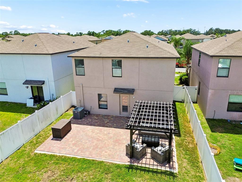 A two-story house exterior features a paved patio with a pergola and white vinyl fencing — 13917 ARBOR PINES DRIVE, RIVERVIEW, FL