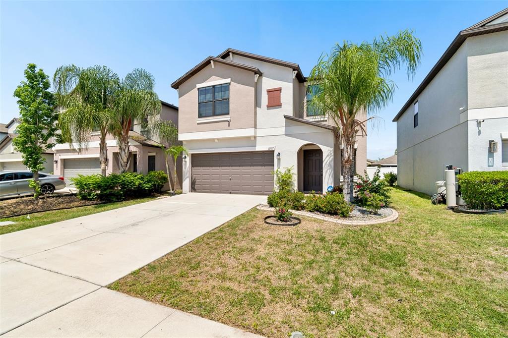 A two-story suburban house features a tan stucco exterior, a two-car garage, and palm trees — 13917 ARBOR PINES DRIVE, RIVERVIEW, FL