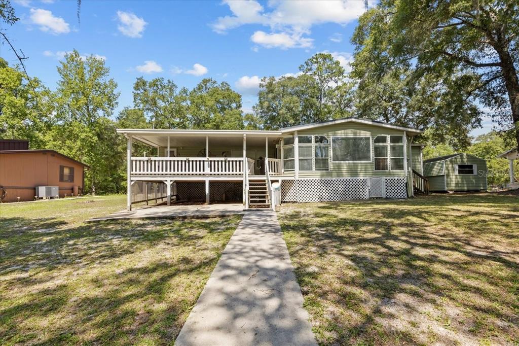 A light green manufactured home features a large elevated wooden deck and a concrete walkway — 9859 NW 38TH TERRACE, BRANFORD, FL