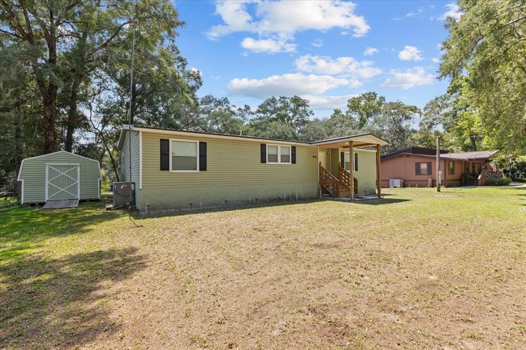 A light green mobile home with a small shed and wooden porch sits on grass — 9859 NW 38TH TERRACE, BRANFORD, FL