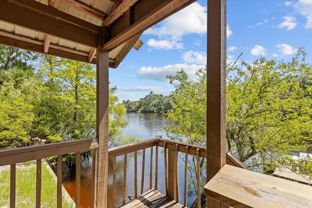 A wooden deck overlooks a river surrounded by lush green trees under a blue sky — 9859 NW 38TH TERRACE, BRANFORD, FL