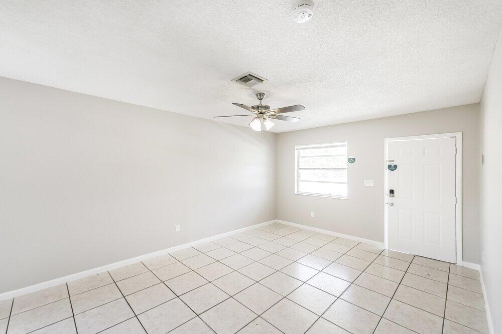 An empty room with light-colored walls, tile flooring, a ceiling fan, and a white door — HALLANDALE BEACH, FL