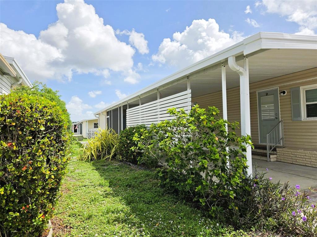 A side view of a manufactured home with a carport, privacy screen, and landscaping — 3227 BAYBERRY TERRACE, SARASOTA, FL