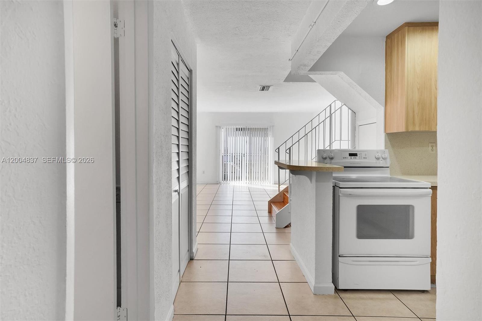 A kitchen with a white stove and tile flooring opens into a living area — 8650 SW 67th Ave # 1025, Pinecrest FL 33156, PINECREST, FL