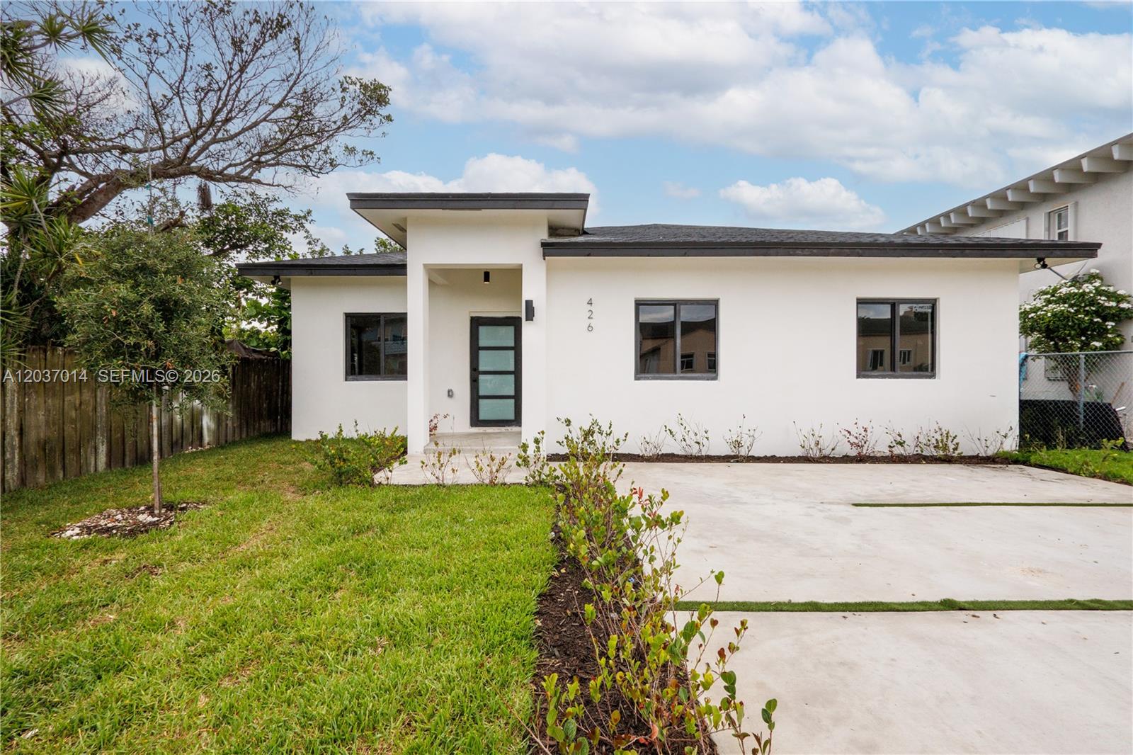 A modern, white single-story house features a flat roof, dark-framed windows, and a concrete driveway — 426 SW 9th Ave, Homestead FL 33030, HOMESTEAD, FL