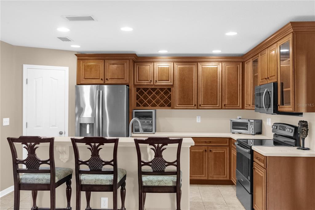 A kitchen features wood cabinets, stainless steel appliances, a breakfast bar, and three wooden chairs — 2916 ROYAL TUSCAN LANE, VALRICO, FL