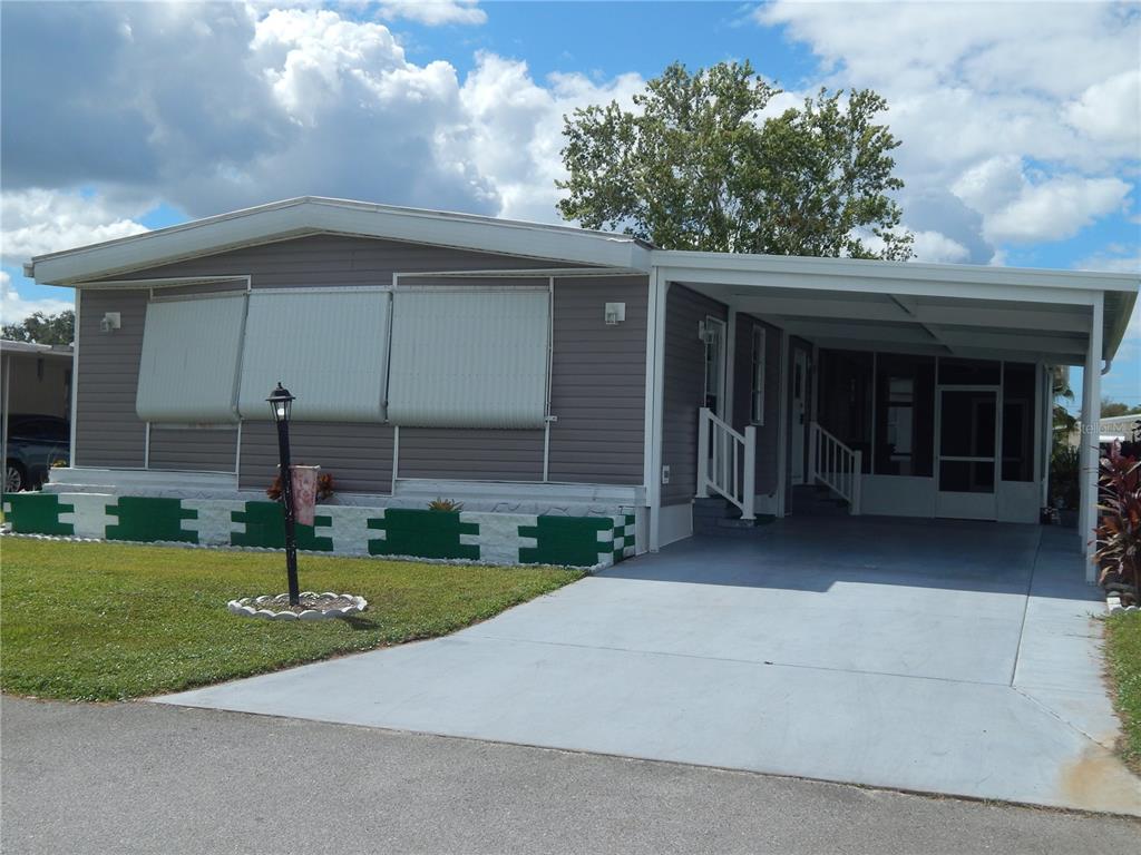 A single-story manufactured home with grey siding, a carport, and a green-trimmed brick foundation — 6710 36TH AVENUE E UNIT 34, PALMETTO, FL