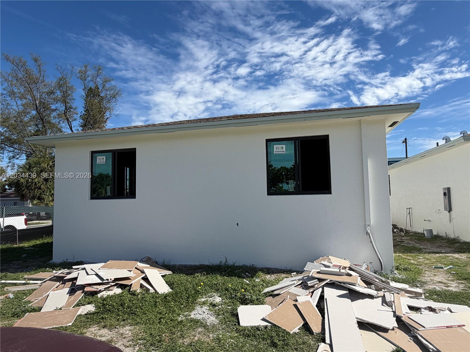 The exterior of a white house features two dark-framed windows and construction debris on grass — 344 NW 11th St, Pompano Beach FL 33060, POMPANO BEACH, FL
