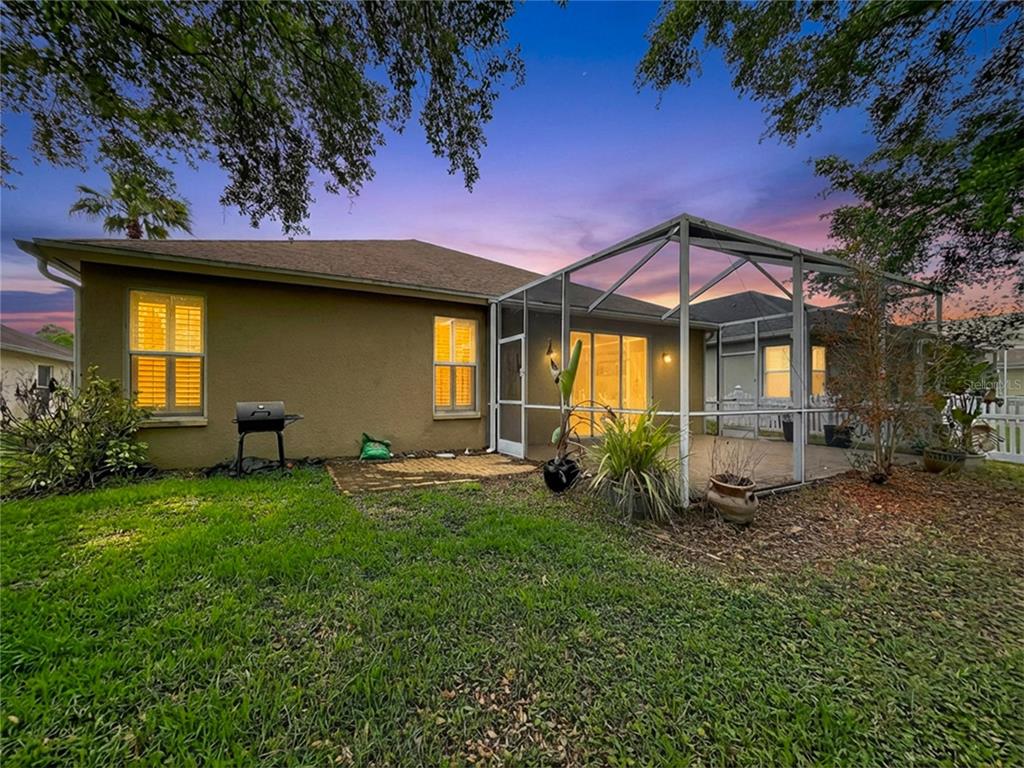 A backyard view of a house with a screened-in patio and a small charcoal grill — 27509 EDENFIELD DRIVE, WESLEY CHAPEL, FL