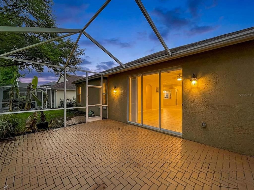 A screened-in patio with brick pavers and sliding glass doors leading into a house — 27509 EDENFIELD DRIVE, WESLEY CHAPEL, FL