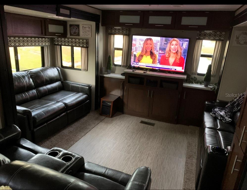A living room inside an RV features dark leather sofas, a television, and wood cabinetry — 650 CENTER CREST BOULEVARD, DAVENPORT, FL