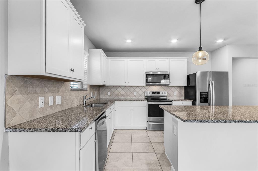 A kitchen features white cabinets, granite countertops, stainless steel appliances, and a tile backsplash — 16033 BEACHBERRY DRIVE, NORTH FORT MYERS, FL