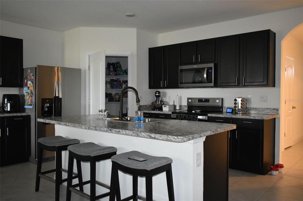 A kitchen features dark cabinets, granite countertops, a center island with bar stools, and stainless appliances — 476 BOARDWALK AVENUE, HAINES CITY, FL