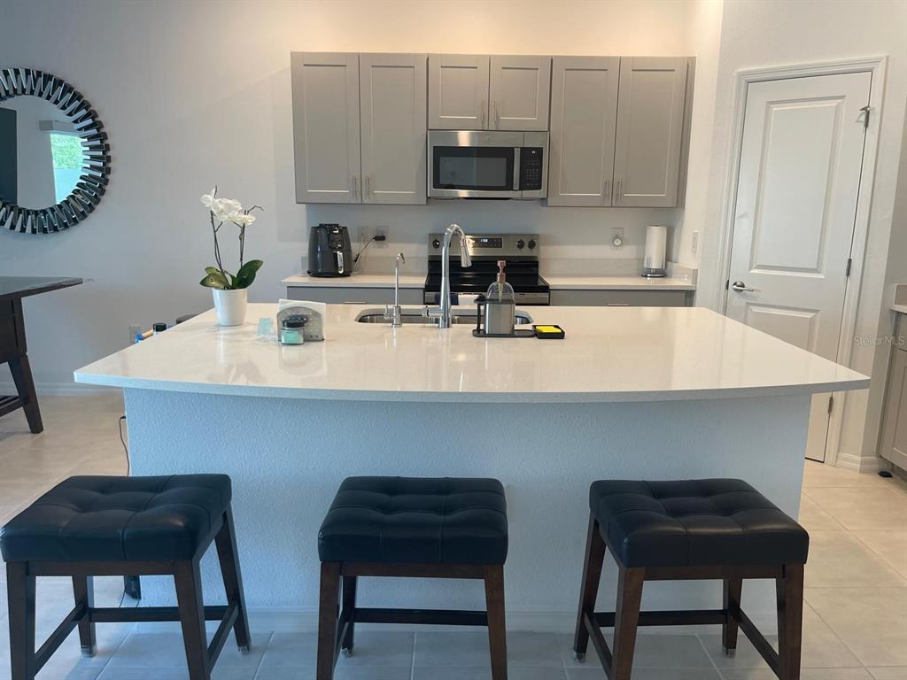 A kitchen features a large white quartz island with three stools and gray cabinets — 2561 PENGUIN BOULEVARD, DAVENPORT, FL