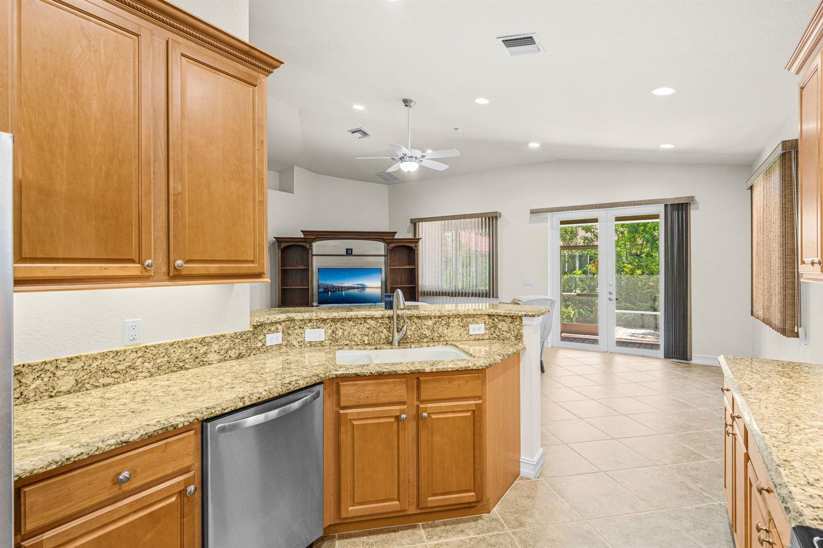 A kitchen with wood cabinets and granite countertops overlooks a living area with glass doors — 6223 Dorchester Way, Vero Beach FL 32966, VERO BEACH, FL