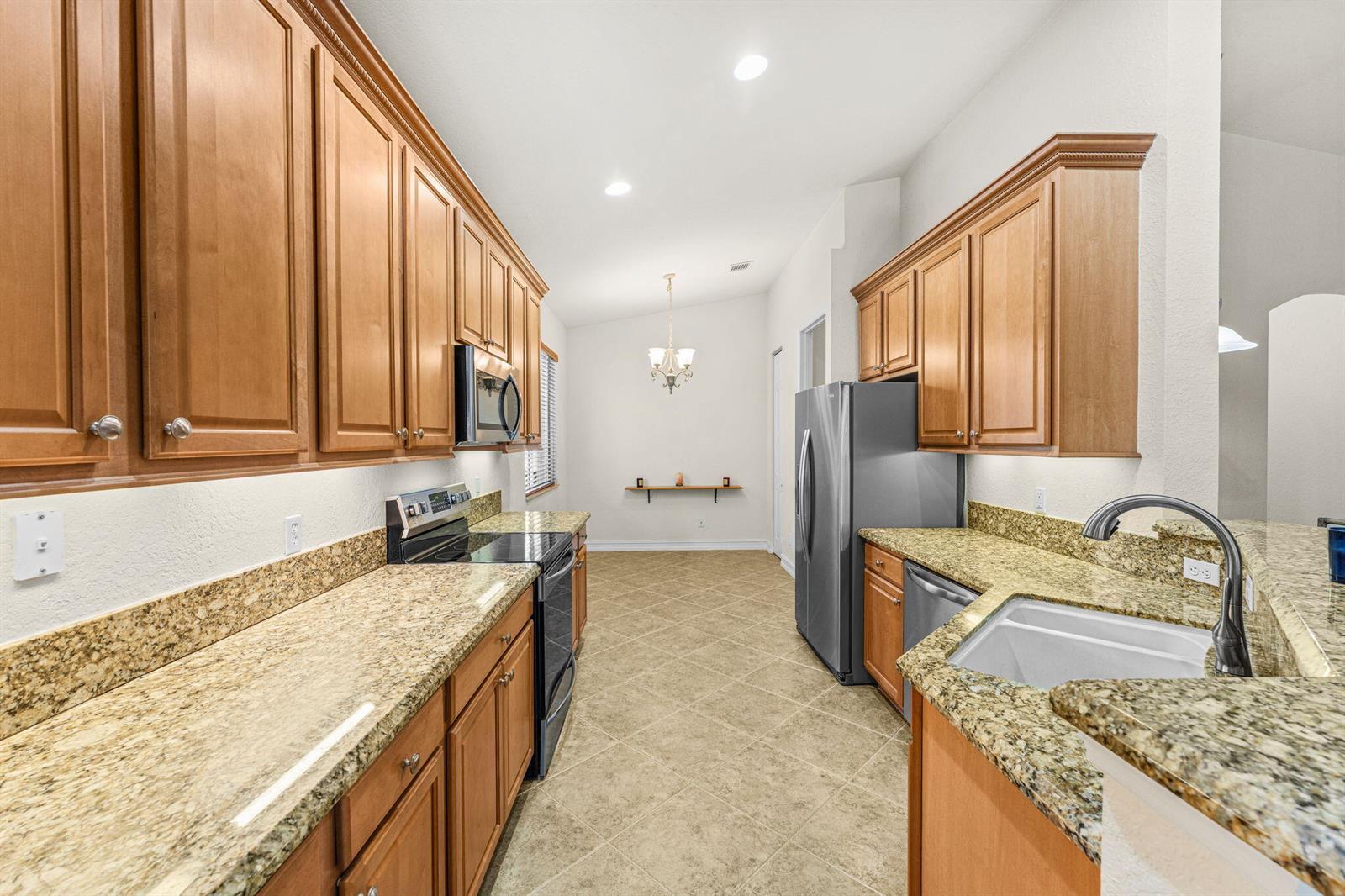 A kitchen features wood cabinets, granite countertops, stainless steel appliances, and a tiled floor — 6223 Dorchester Way, Vero Beach FL 32966, VERO BEACH, FL