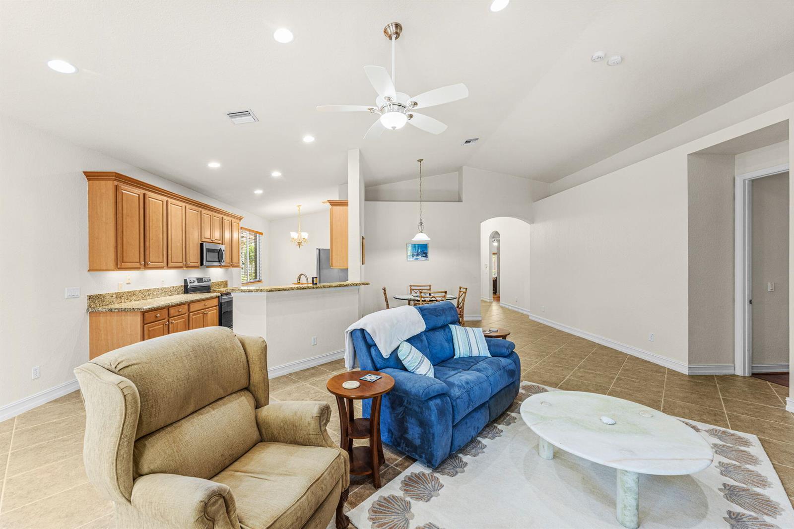 An open-concept living room features tile flooring, a blue sofa, and an adjacent kitchen area — 6223 Dorchester Way, Vero Beach FL 32966, VERO BEACH, FL