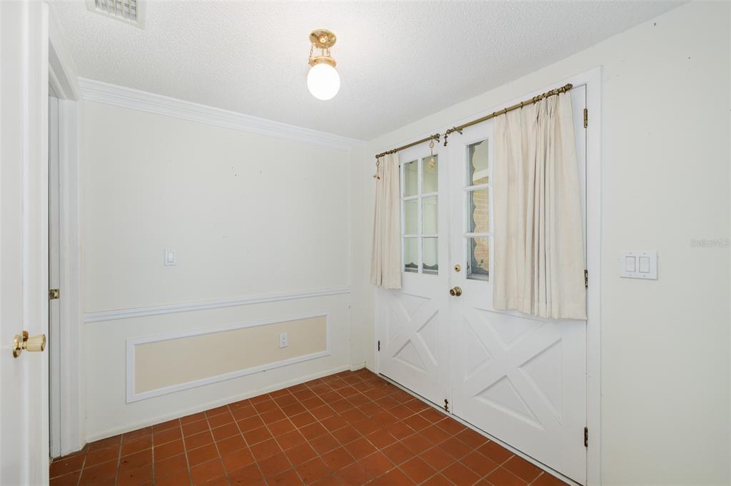 An entryway with terracotta tile flooring, white wainscoting, and double doors with glass panels — 8315 CAVALRY DRIVE, HUDSON, FL