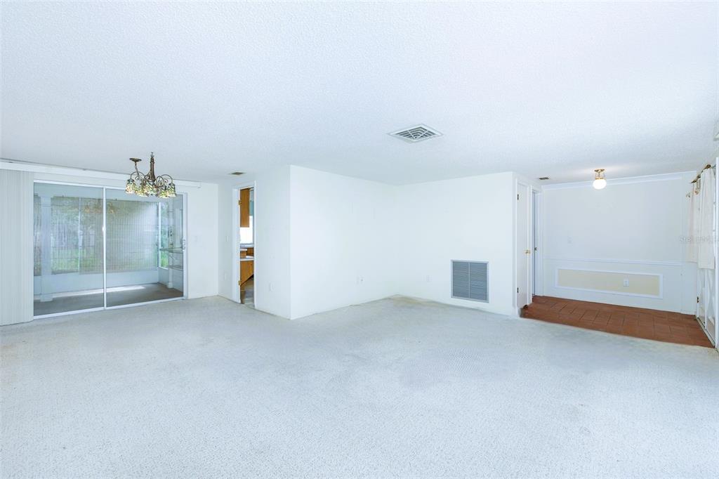 A spacious living room with white carpet, a sliding glass door, and a tiled entryway — 8315 CAVALRY DRIVE, HUDSON, FL