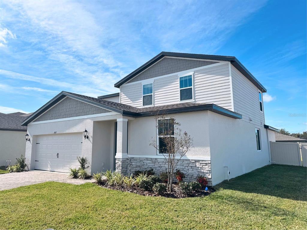 A two-story suburban house features a stucco and stone exterior with a two-car garage — 1887 DRAUGHTON DRIVE, ZEPHYRHILLS, FL