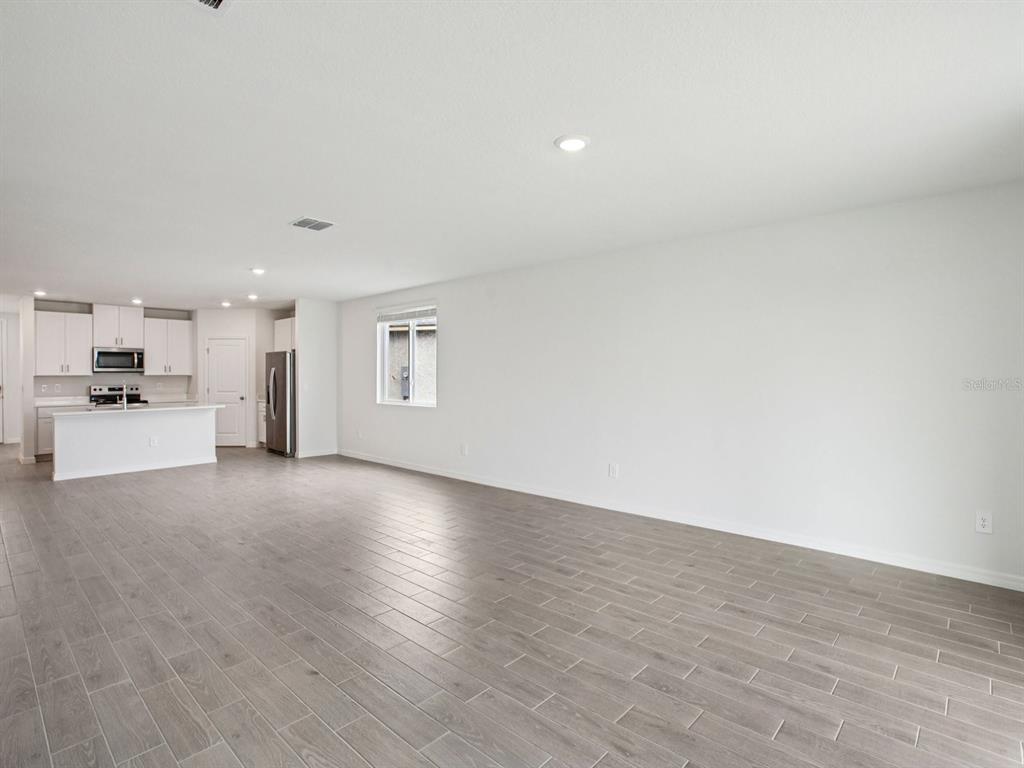 An open-concept living area features light gray tile flooring, white walls, and a kitchen island — 1887 DRAUGHTON DRIVE, ZEPHYRHILLS, FL