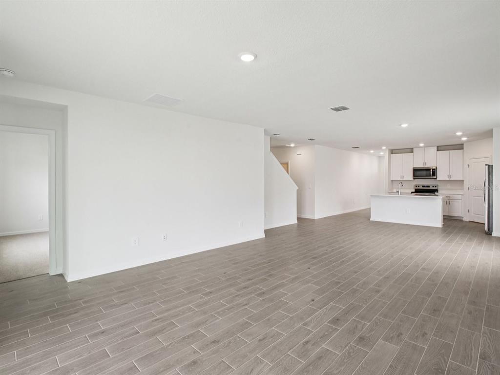 An open-concept living area features gray wood-look tile flooring, white walls, and a modern kitchen — 1887 DRAUGHTON DRIVE, ZEPHYRHILLS, FL