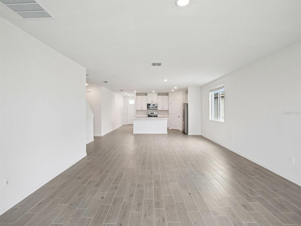 An open-concept living area features light gray wood-look tile flooring and a white kitchen — 1887 DRAUGHTON DRIVE, ZEPHYRHILLS, FL