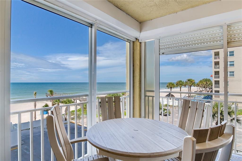 A screened-in balcony features a round table and chairs overlooking the ocean and beach — 17450 GULF BOULEVARD UNIT 206, REDINGTON SHORES, FL