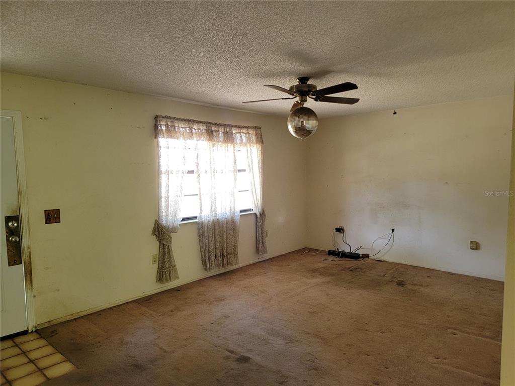 An empty living room features beige carpeting, a ceiling fan with a disco ball light, and curtains — 2240 GABARONE BOULEVARD, AUBURNDALE, FL