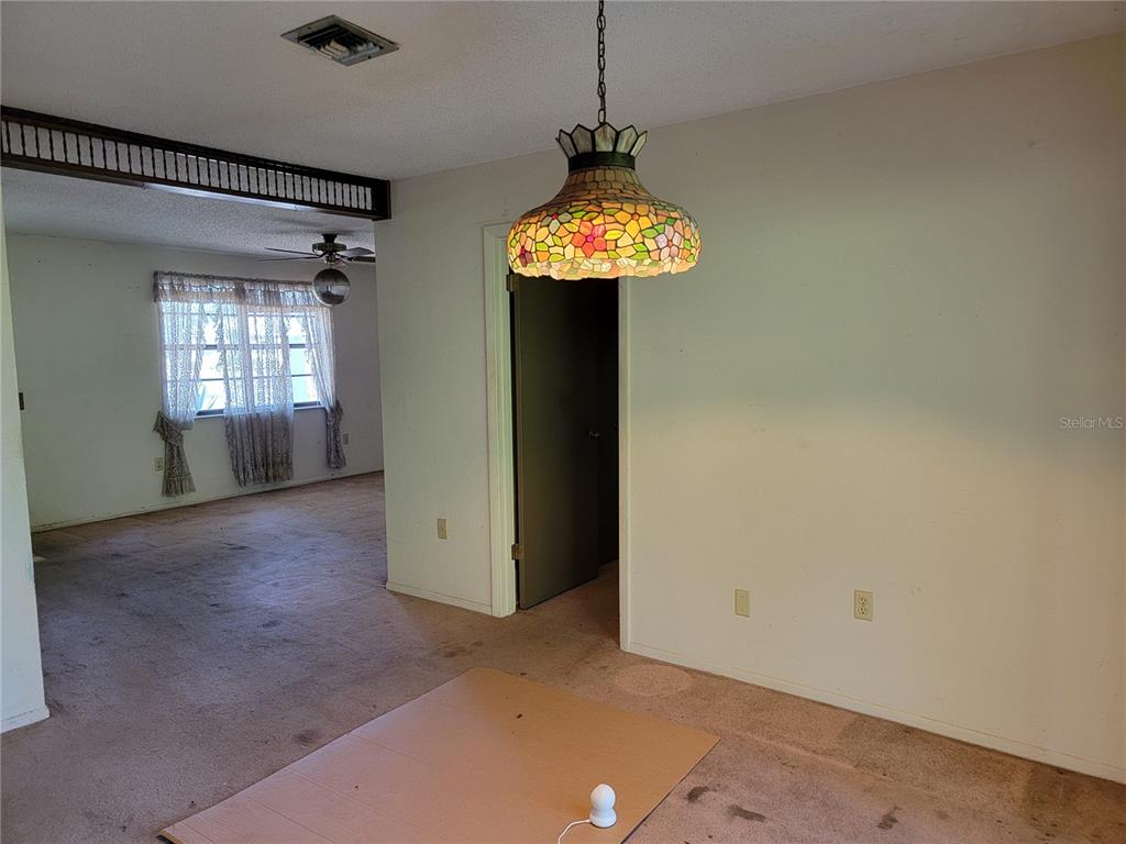 A dining area features a stained-glass pendant light, beige carpeting, and an adjacent living room — 2240 GABARONE BOULEVARD, AUBURNDALE, FL