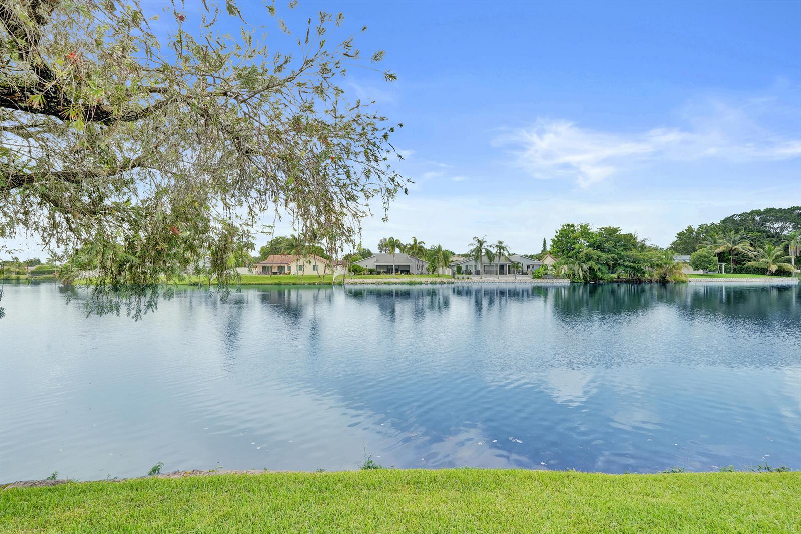 A view of a calm lake with residential houses in the background under a blue sky — 1122 NW 79th Drive, Plantation FL 33322, PLANTATION, FL