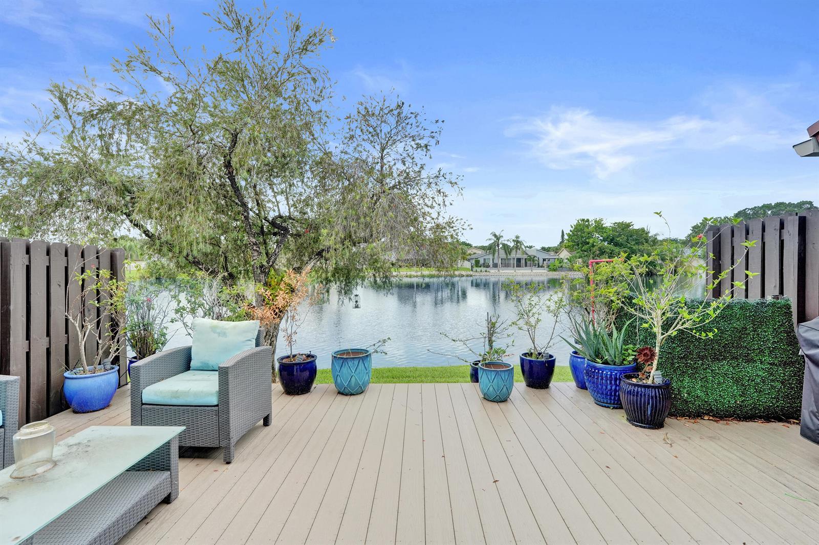 A wooden deck overlooks a lake with potted plants and outdoor furniture — 1122 NW 79th Drive, Plantation FL 33322, PLANTATION, FL